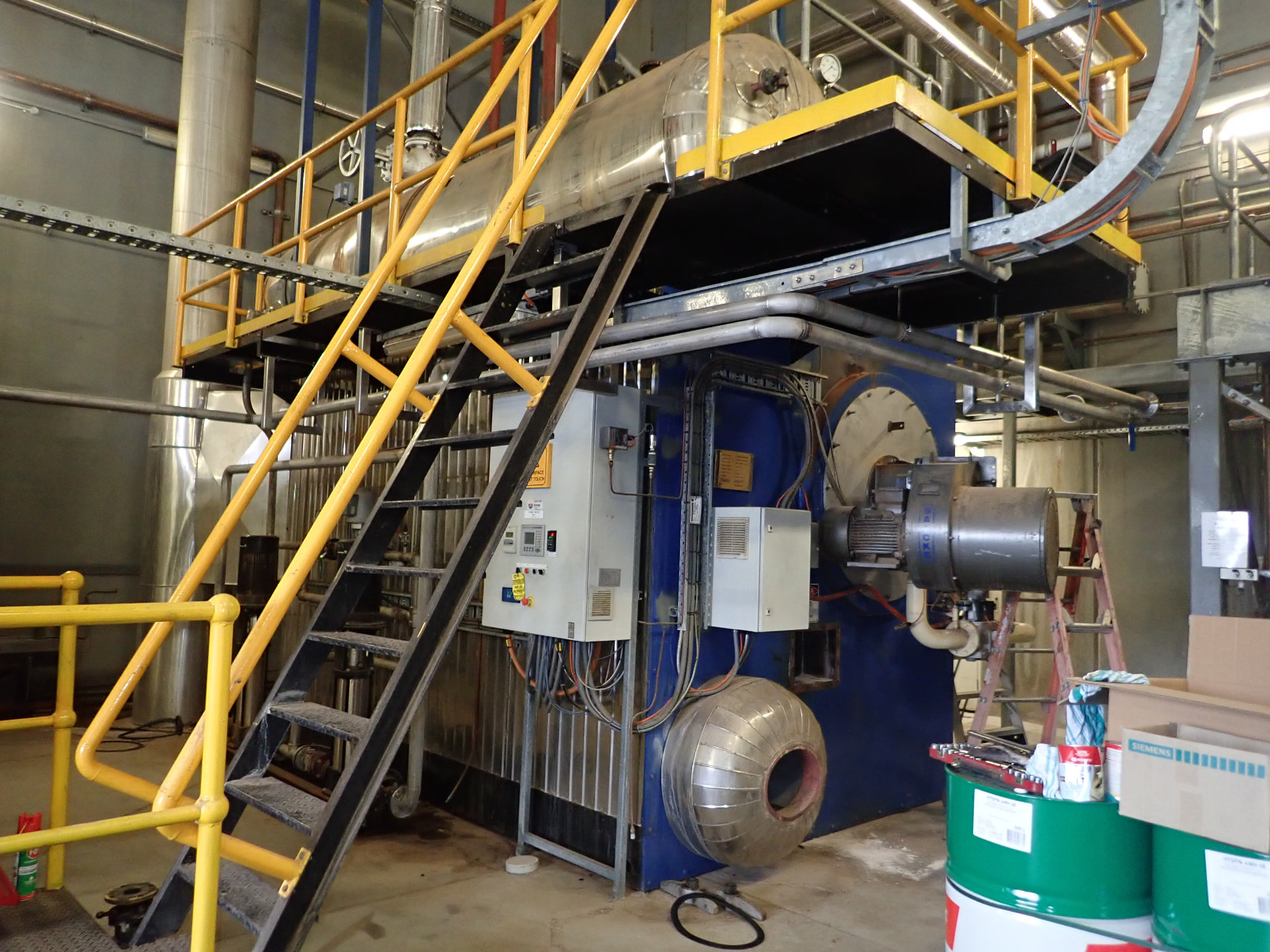 Industrial boiler and pressure vessel with yellow access platforms, pipework and electrical panels in a manufacturing facility