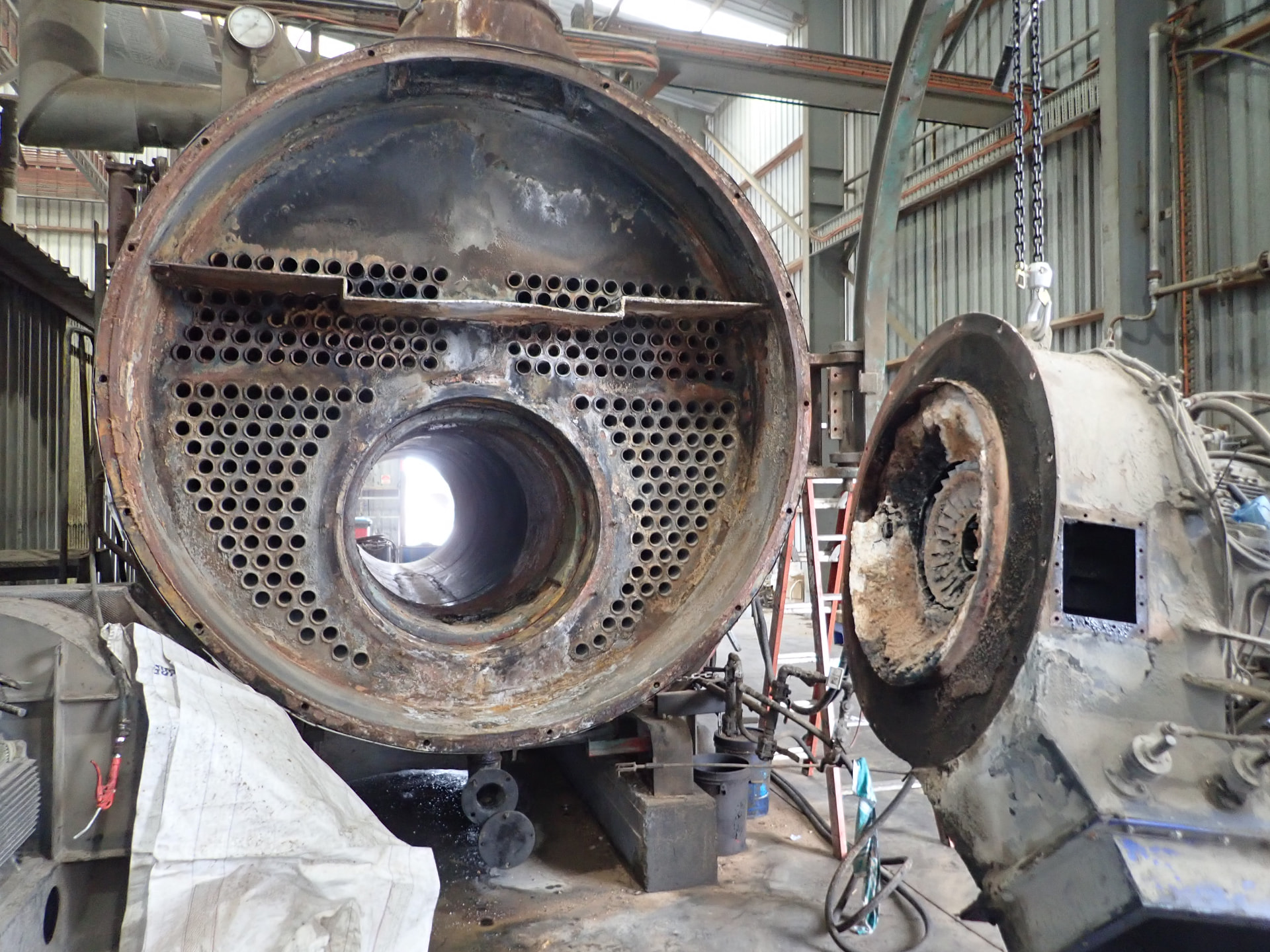 Industrial fire-tube boiler in a workshop with the end cover removed, revealing the tube bundle and pressure vessel internals